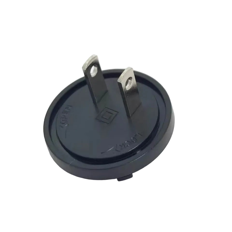 A black circular electrical plug adapter with two metal pins, photographed on a plain white background.